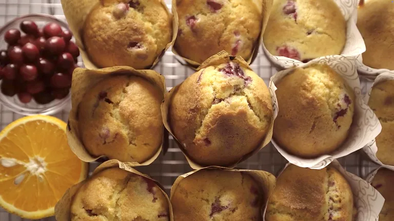 Golden cranberry orange muffins with cracked tops in a muffin tin, cooling on a wire rack.