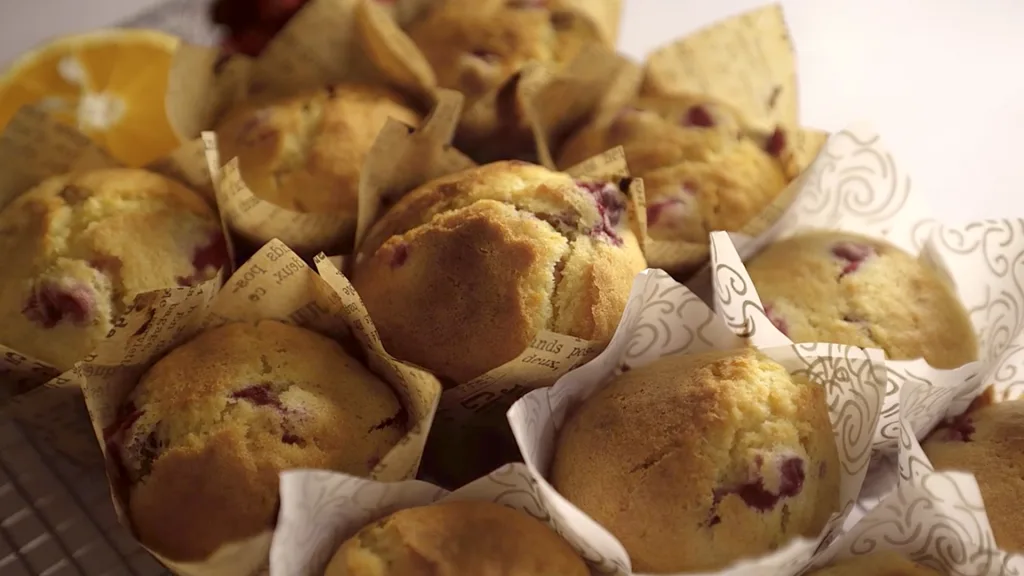 Golden cranberry orange muffins with cracked tops in a muffin tin, cooling on a wire rack.