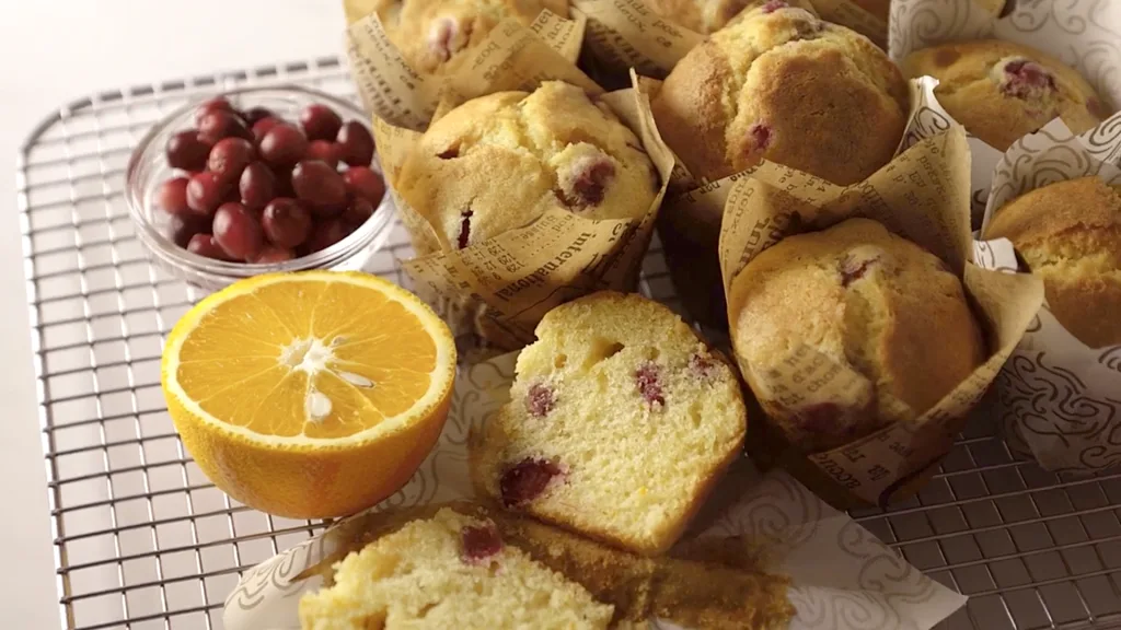 Golden cranberry orange muffins with cracked tops in a muffin tin, cooling on a wire rack.