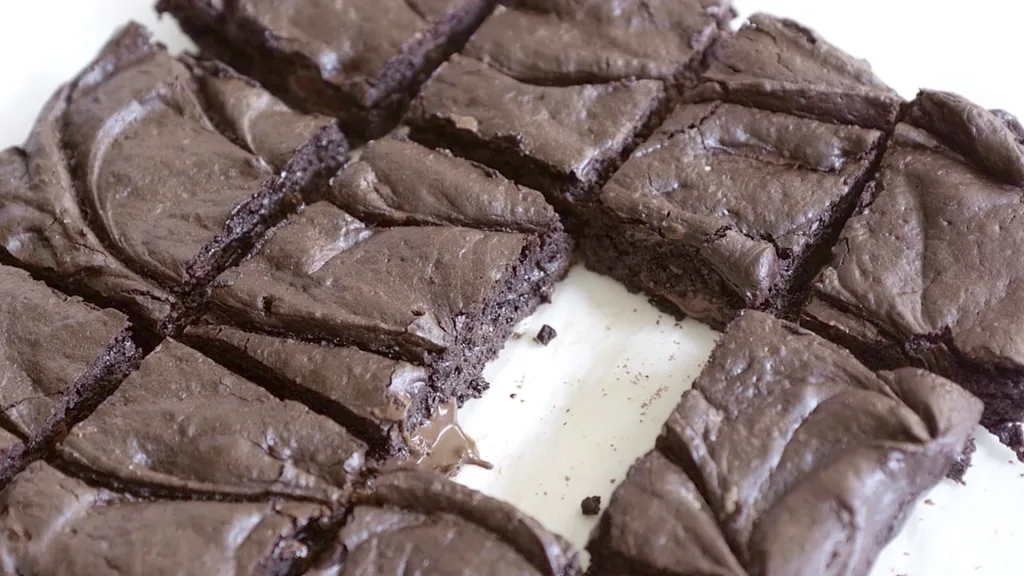 Close-up of sliced fudgy brownies on parchment paper, showing crackly tops and rich, dense centers.
