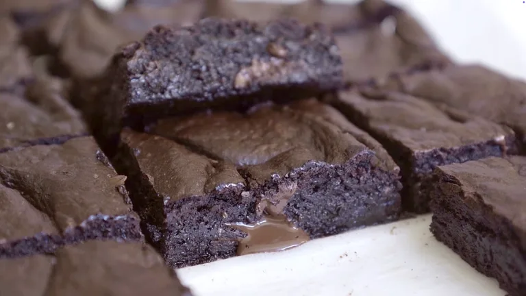 Close-up of sliced fudgy brownies on parchment paper, showing crackly tops and rich, dense centers.