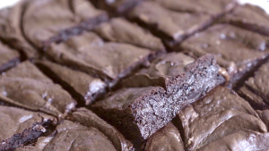 Close-up of sliced fudgy brownies on parchment paper, showing crackly tops and rich, dense centers.
