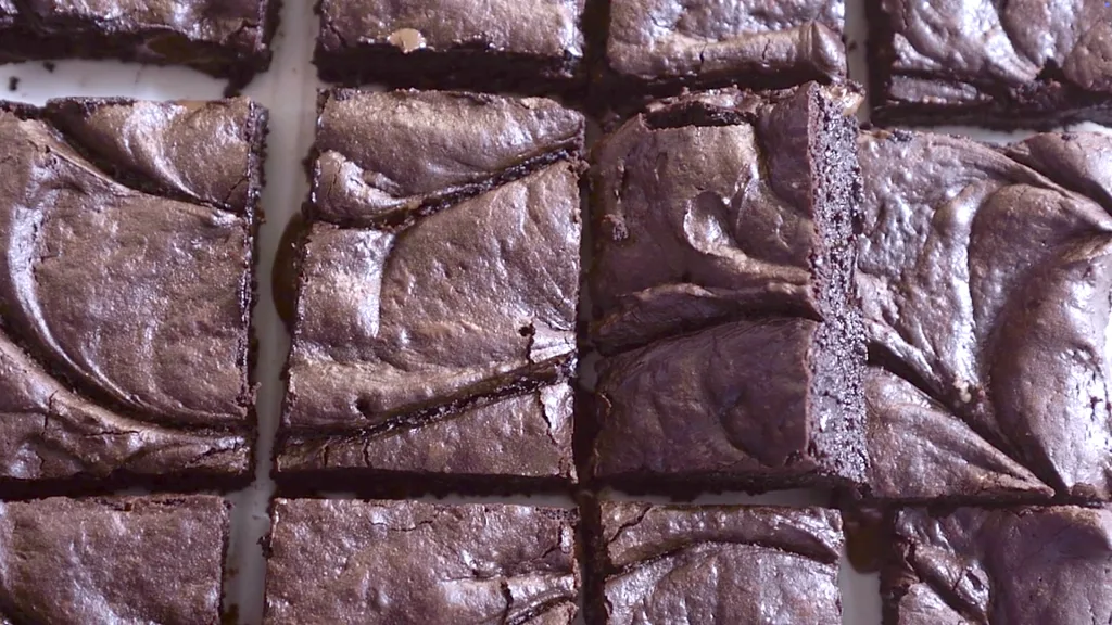 Close-up of sliced fudgy brownies on parchment paper, showing crackly tops and rich, dense centers.