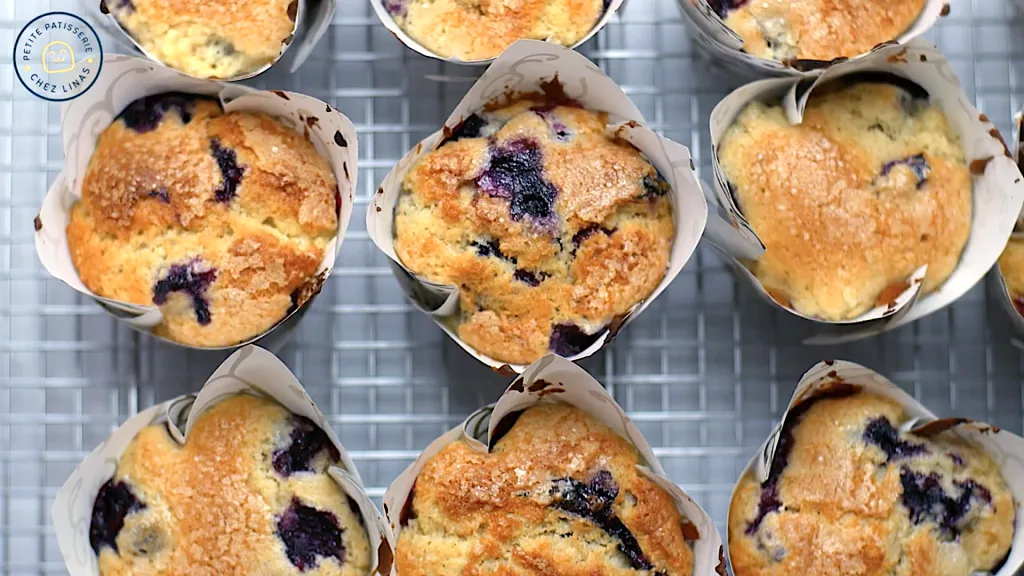 Close-up of golden-topped Jordan Marsh blueberry muffins cooling on a wire rack.