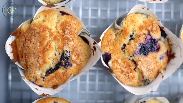 Close-up of golden-topped Jordan Marsh blueberry muffins cooling on a wire rack.
