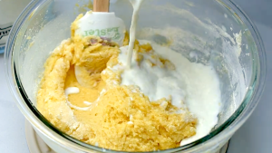 Creamy blueberry muffin batter being mixed in a glass bowl.