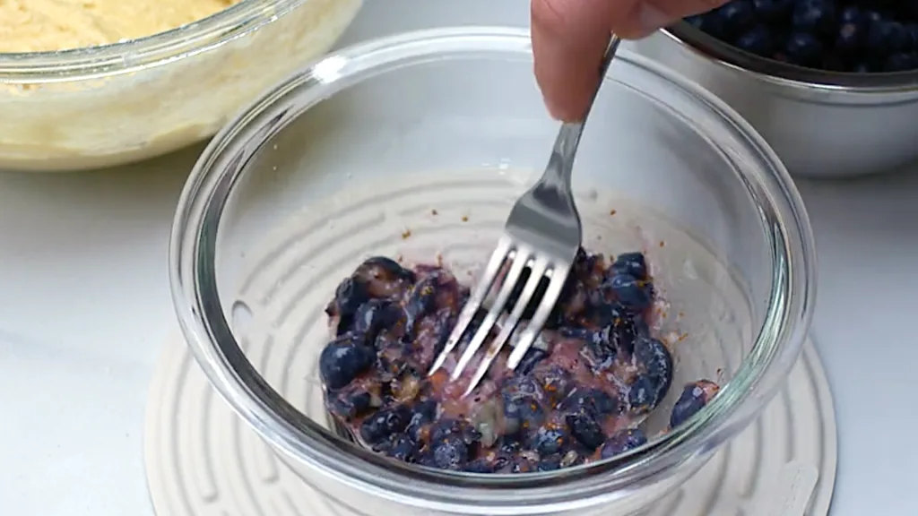 Mashed blueberries in a bowl, ready to be folded into muffin batter.