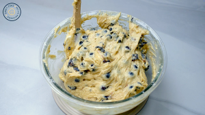 Creamy blueberry muffin batter being mixed in a glass bowl.