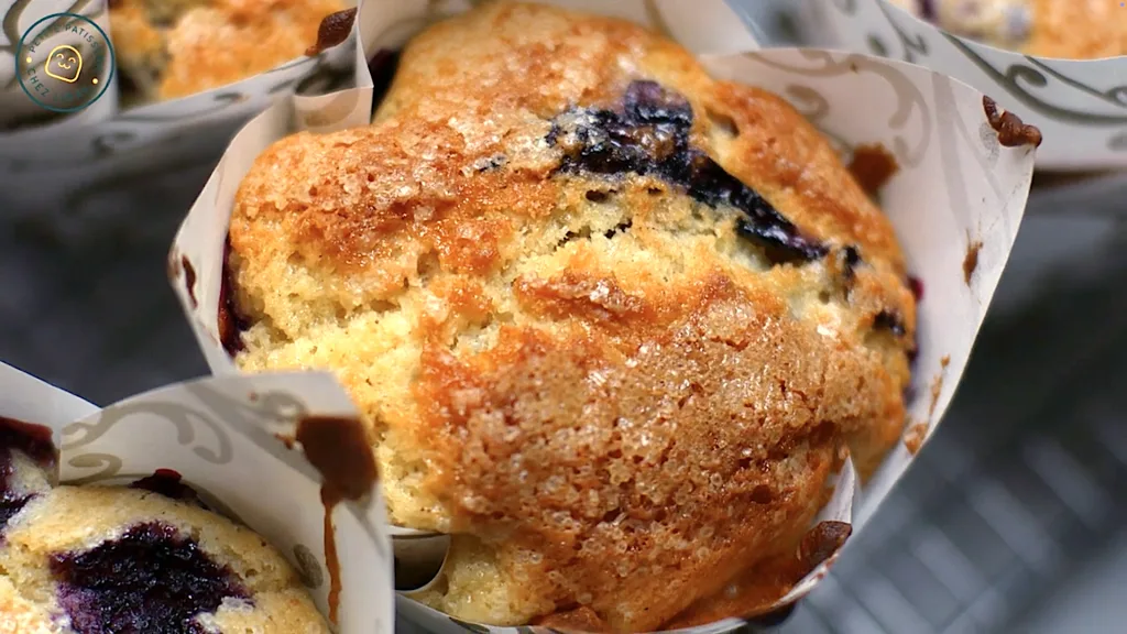 Close-up of golden-topped Jordan Marsh blueberry muffins cooling on a wire rack.