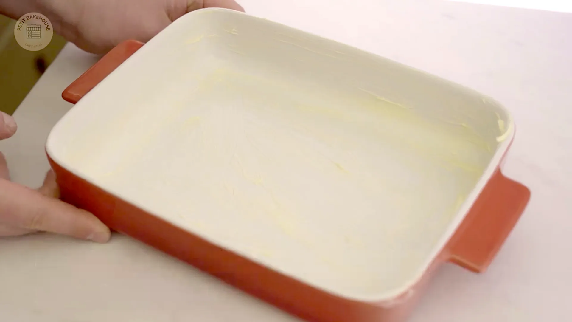Empty baking dish being greased with butter, oven preheating in background